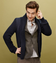 Tom Mison in a blue cardigan scratching his ear